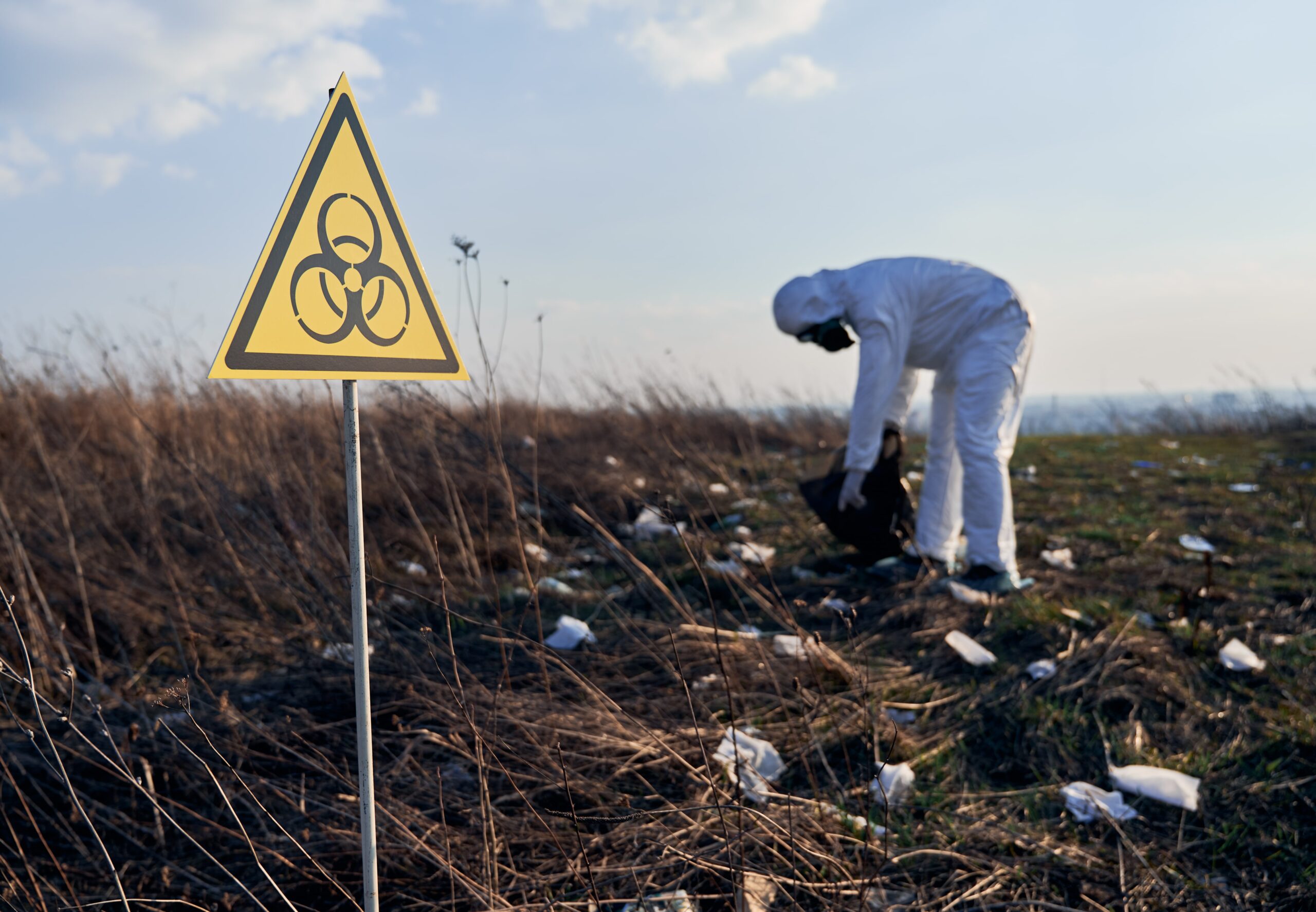 researcher-protective-suit-collecting-plastic-garbage-into-black-waste-bag-outdoors-sunny-day-min